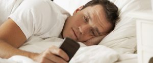 Man In Bed At Home Texting On Mobile Phone